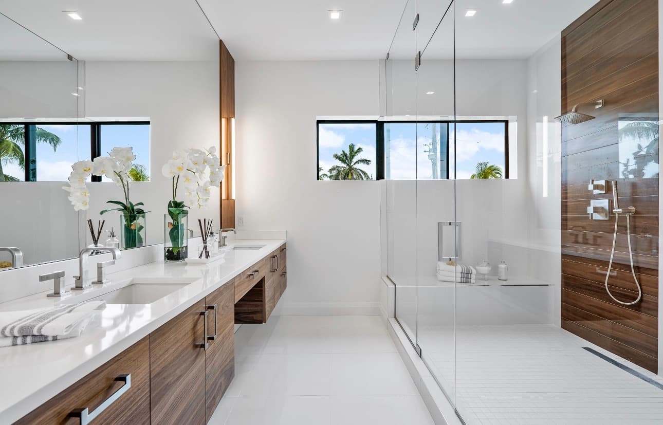 Modern bathroom with walnut double vanity, glass walk-in shower with wood accent wall, and tropical views