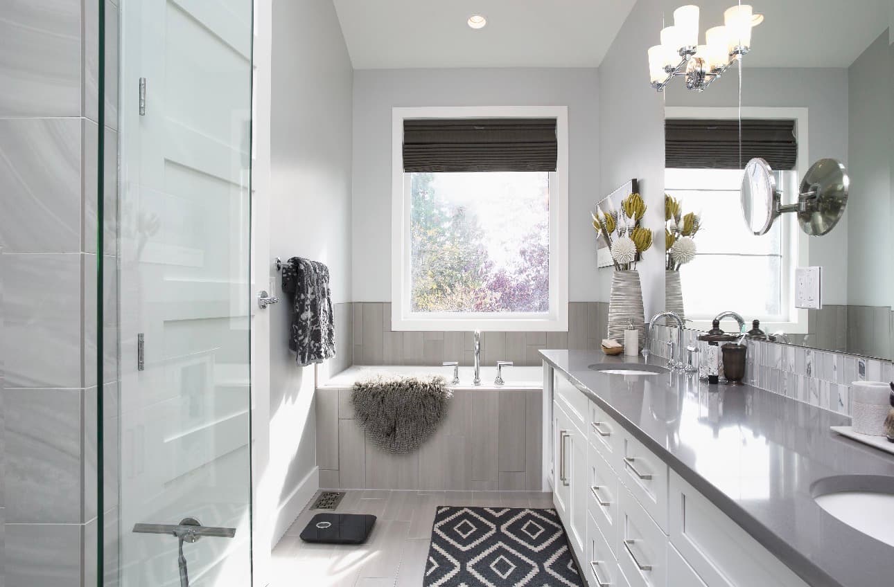 Transitional bathroom with built-in tub by window, long white vanity with gray countertop, and chandelier